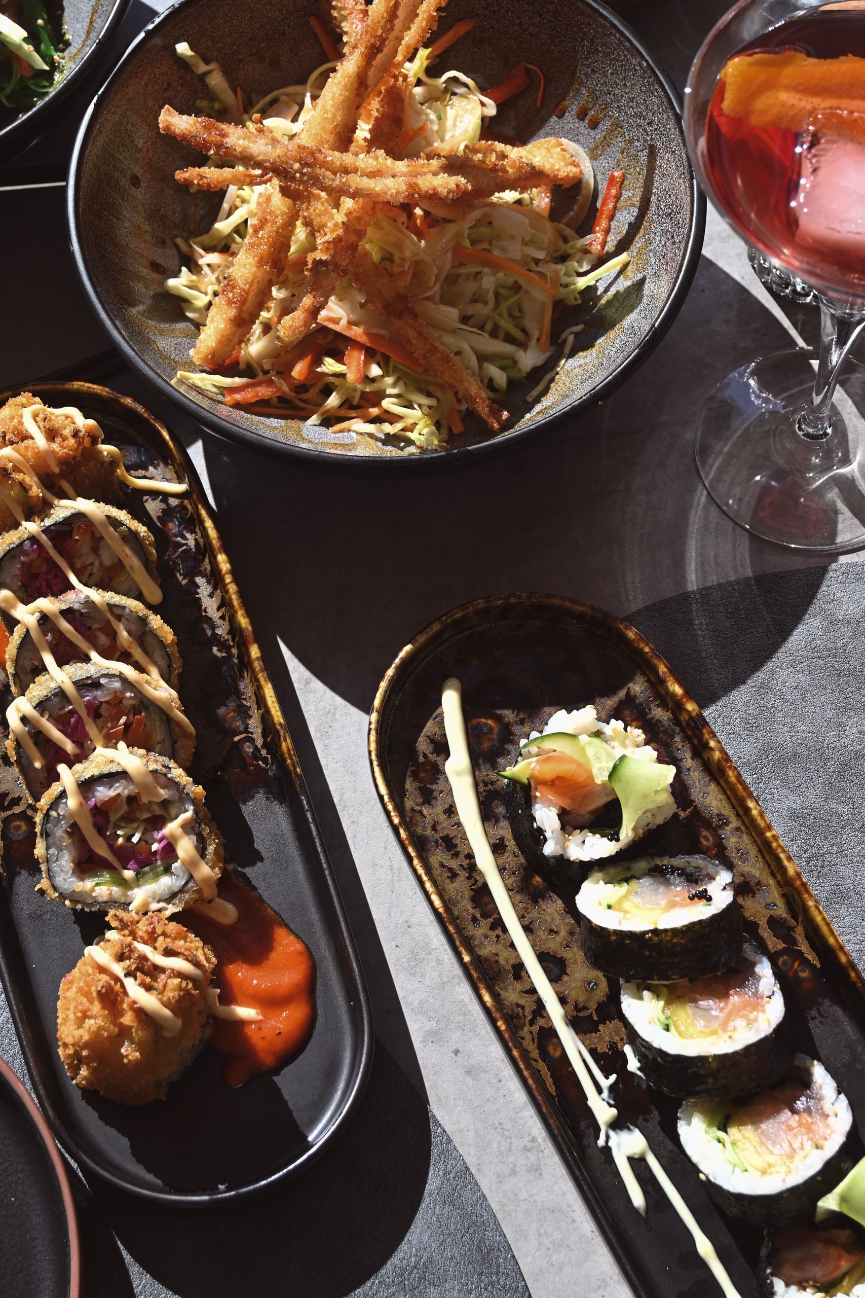 Κάτοψη με τηγανητά λαχανικά tempura σε μπολ και ρολά sushi με σάλτσα σε σκούρες πλατέλες.